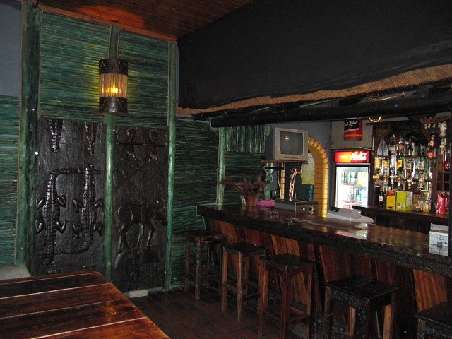 The bar counter with wooden stools, drinks fridges and carved panels behind
